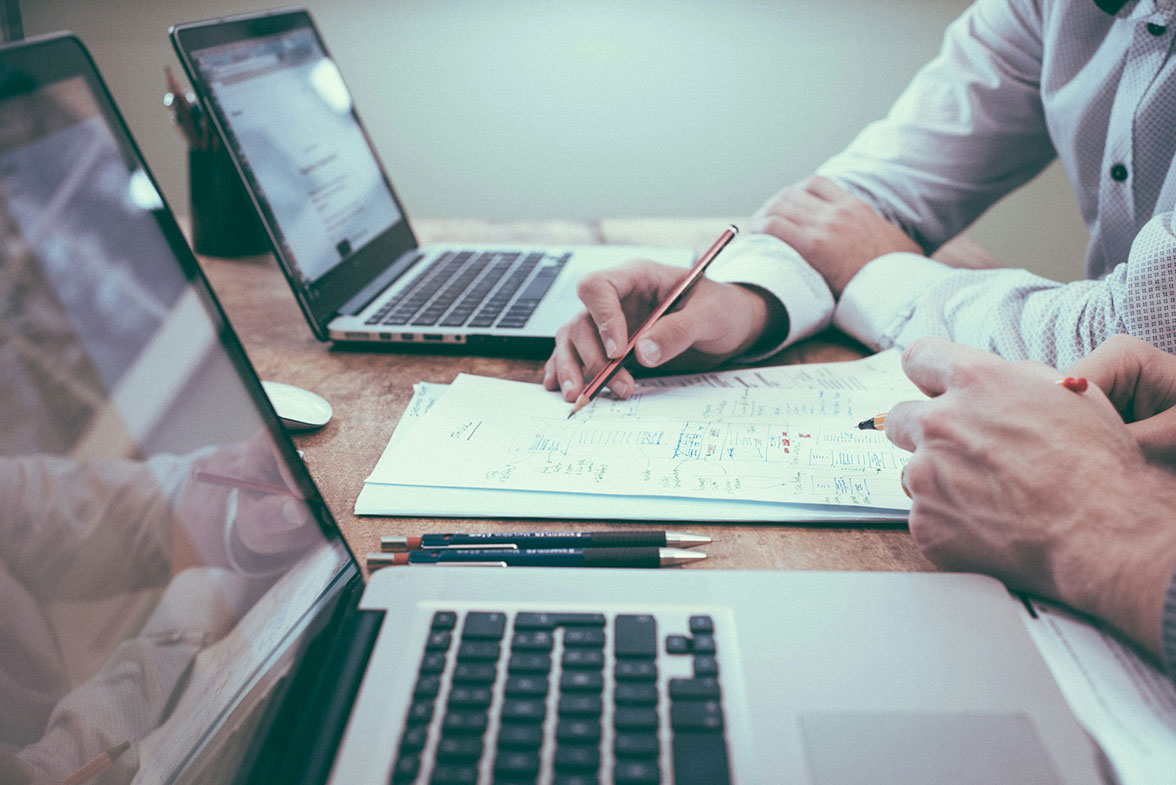 Two professionals discussing financial planning with documents and laptops on a desk.
